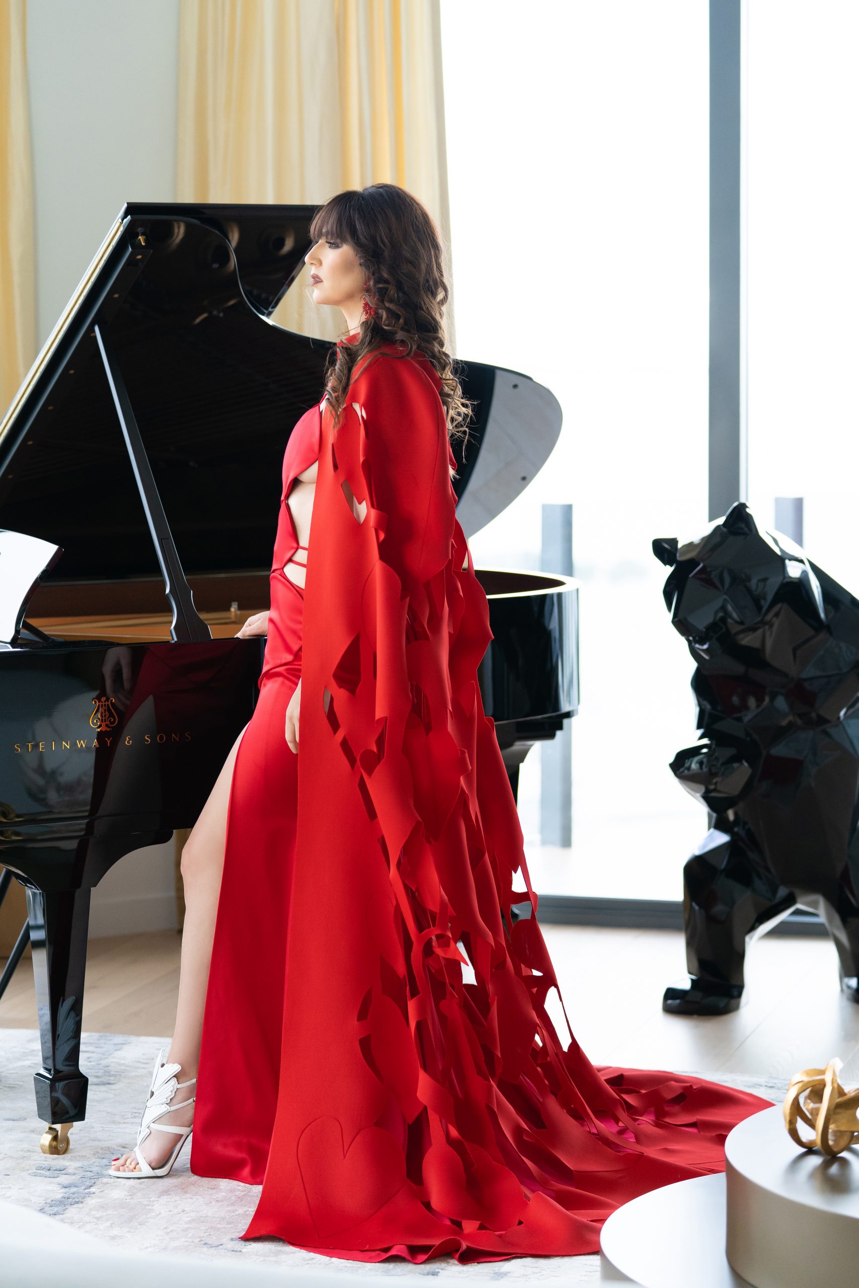 Radmila Lolly standing beside a Piano wearing a red Dress